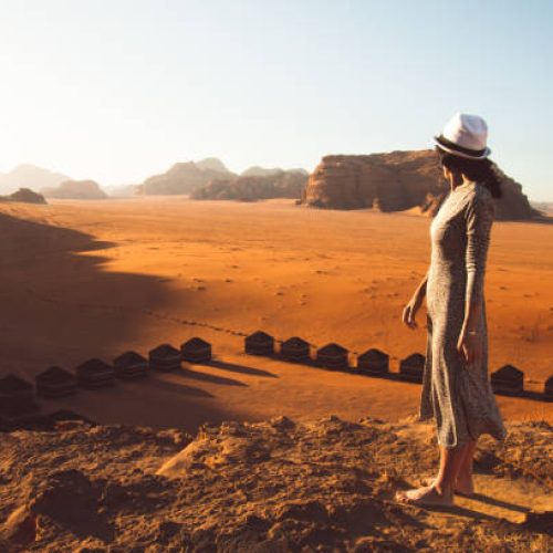 Slim beautiful caucasian woman tourist stand on cliff barefoot watch sunrise and enjoy holiday vacation in Wadi rum panorama by bedouin campsite. Popular Wadi Rum desert in Jordan